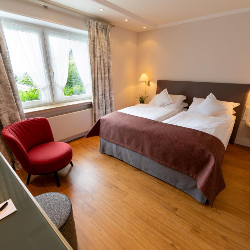 Zimmer 51: Schönes Bett im Doppelzimmer mit rotem Sessel, Schreibtisch und Höckerchen